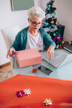 Woman wrapping Christmas presents, looking at her phone