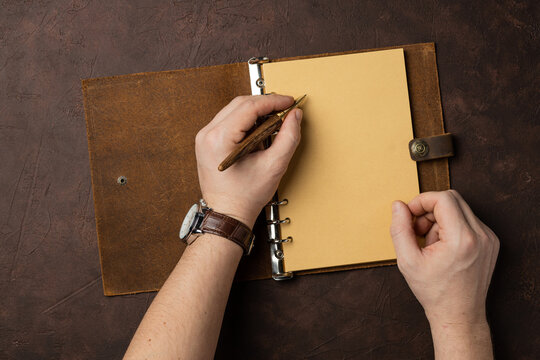 male hands writing in notebook or diary on brown background