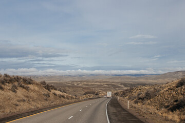 A beautiful landscape with a highway along which cars and trucks drive, on a sunny autumn day among the mountains, a blue sky with fluffy gray-blue clouds. Oregon, USA, 12-5-2019