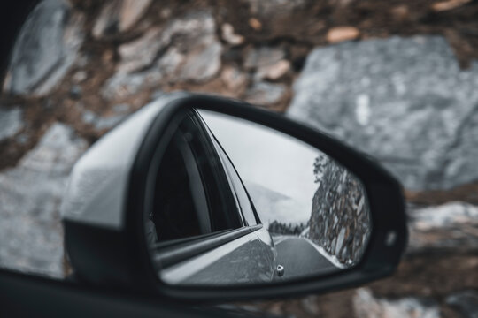 Side-view mirror reflection of car driving along alpine highway