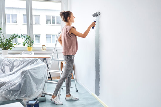 Young woman painting with paint roller on wall while standing at home