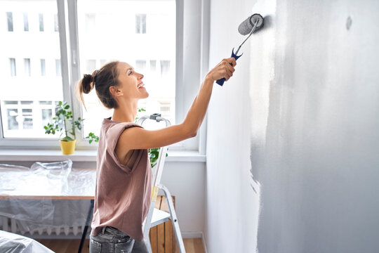 Smiling woman painting wall with paint roller while standing at home