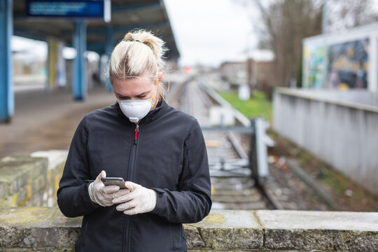 Teenage girl wearing protective mask and gloves using cell phone while waiting at train station