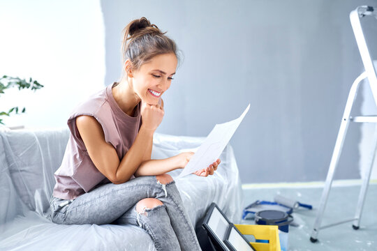 Smiling woman with head in hands reading paper while sitting on sofa at home