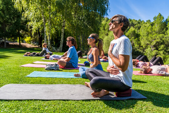 Mature male and female tourists practicing yoga on mat at health retreat during sunny day