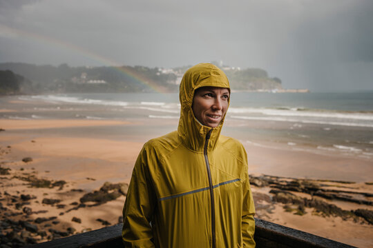 Smiling woman wearing raincoat by retaining wall during rainy season