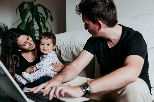 Smiling mother holding son while father working on laptop sitting at home