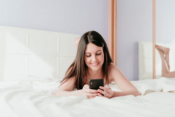 Smiling beautiful woman text messaging while lying on bed at home