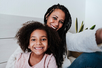Happy mother and daughter sitting on bed in bedroom at home