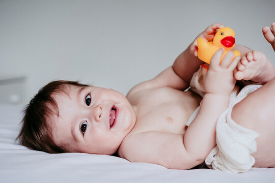Smiling cute baby boy playing with duck toy while lying down on bed at home