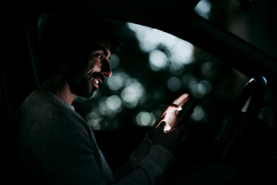 Smiling Man Using Mobile Phone While Sitting In Car At Night