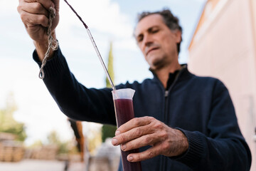 Male winemaker measuring temperature of wine through thermometer at winery