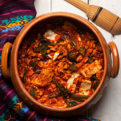 Mexican scrambled eggs in red sauce with poblano pepper and cheese on white background