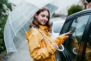 Smiling girl in raincoat holding umbrella while standing by car in city
