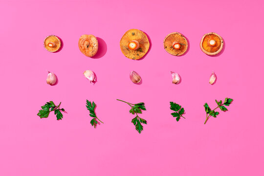 Mushrooms, garlic and parsley arranged on pink background