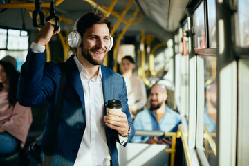Happy businessman listening music over headphones while commuting by bus.