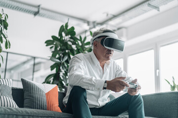 Senior businessman playing video game with virtual reality eyeglasses at office