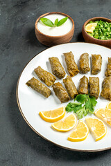bottom view stuffed grape leaves on plate bowls with natural yogurt parsley green pepper slices of lemon on dark background