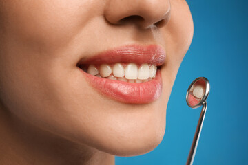 Fototapeta premium Young woman with mouth mirror on blue background, closeup. Cosmetic dentistry