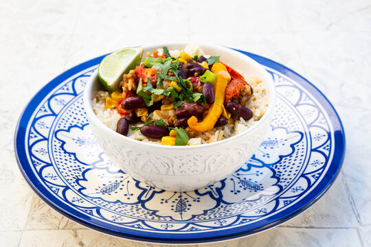 Bowl of Mexican rice with tomatoes, bell pepper, tofu, kidney beans, corn, scallion and lime