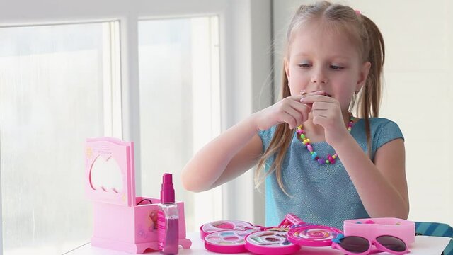 Little beautiful girl puts a ring on her finger. The child plays at home in a toy beauty salon, trying on accessories. A little girl dreams of a wedding.