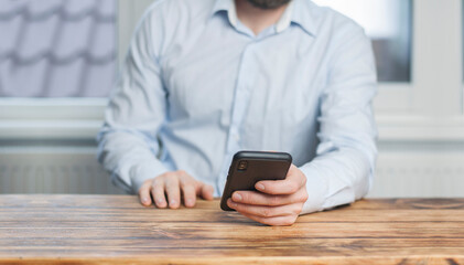 A man with a phone in his hands. Sitting at the table in the office.