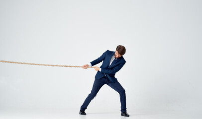 Fototapeta na wymiar business man in a suit pulls a rope on a light background