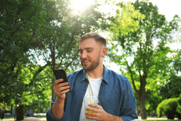 Young man with refreshing drink and smartphone in park