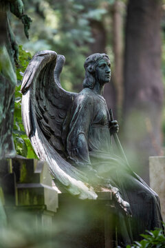 Weathered statue of angel sitting at edge of tomb in cemetery