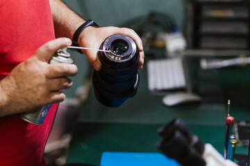 Repairman holding spray can and lens at electronics repair shop