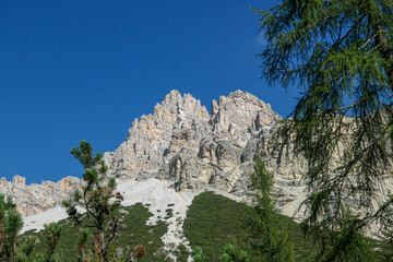 A distant view on a high mountain in Italian Dolomites. It has very steep slopes, full of landslides and lose stones. Thick forest at the foothill of the mountain. A few tree branches on the side