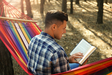 Fototapeta premium Man with book relaxing in hammock outdoors on summer day