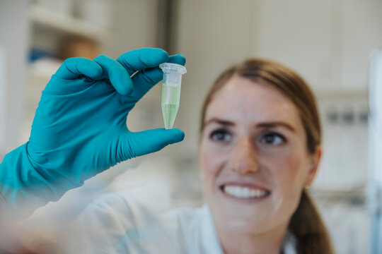 Smiling woman looking at testube while holding in hands at laboratory