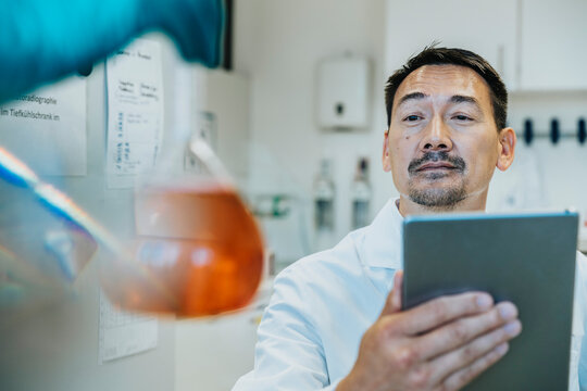 Scientist looking at liquid flask while using digital tablet at laboratory