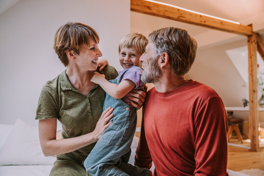 Happy mother cuddling son while father sitting beside on bed at home