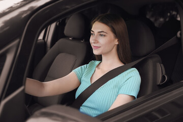 Fototapeta na wymiar Young woman with fastened safety belt on driver's seat in car