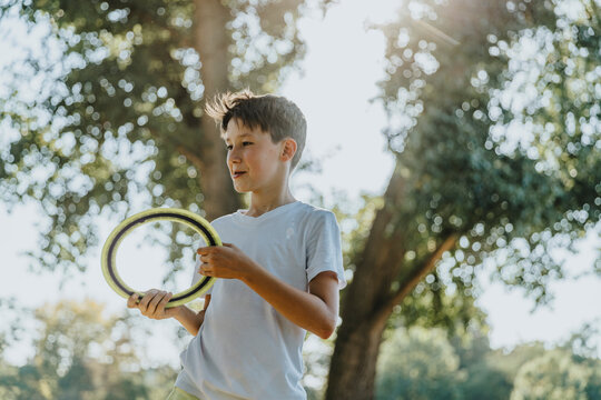 Boy throwing frisbee ring while standing in public park