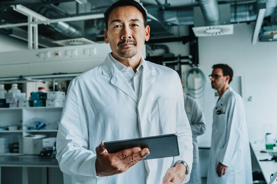 Scientist using digital tablet while standing with coworker in background at laboratory