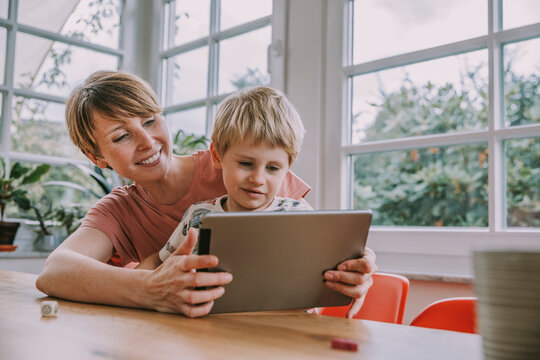 Mother holding digital tablet with son while sitting at home