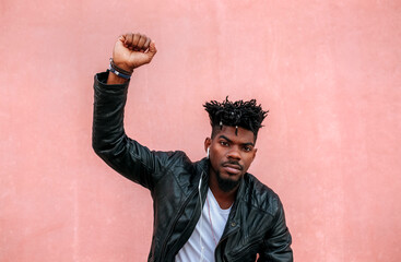Serious man with arm raised listening music while standing against pink wall