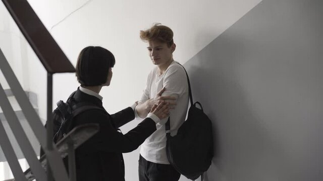 Coquette brunette teenage girl touching shy nerd boy and kissing cheek. Surprised Caucasian redhead high school student looking classmate leaving. First love flirt concept.