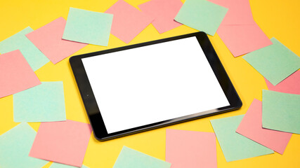 Cropped close up view of mock up image black tablet pc white blank screen isolated yellow bright background. Colorful memo sticky pin clips empty notes scattered in a chaotic manner.