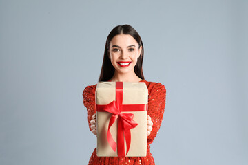 Fototapeta premium Woman in red dress holding Christmas gift on grey background