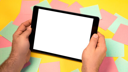 Cropped close up view of mock up image man hand hold black tablet pc white blank screen isolated yellow bright background. Colorful memo sticky pin clips empty notes scattered in a chaotic manner.