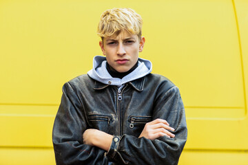 Blond teenage boy standing with arms crossed against yellow van in city