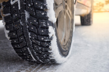 Winter studded tires on snowy road. Wheels of the car standing on winter road. Morning sunlight.