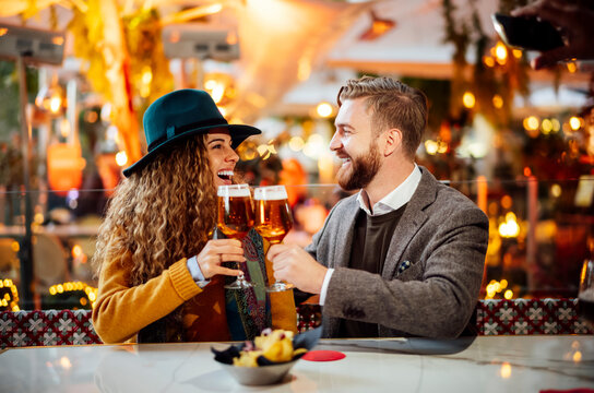 Couple toasting beer while sitting at beer garden in city