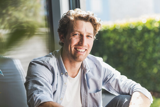 Mid adult man smiling while sitting in house - Powered by Adobe