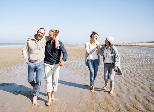 Smiling men waking with women talking in background at beach