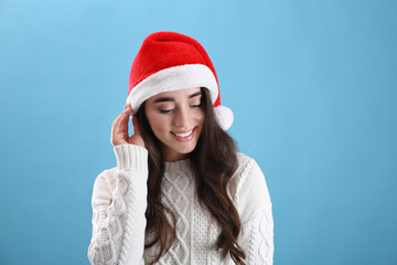 Beautiful woman wearing Santa Claus hat on light blue background